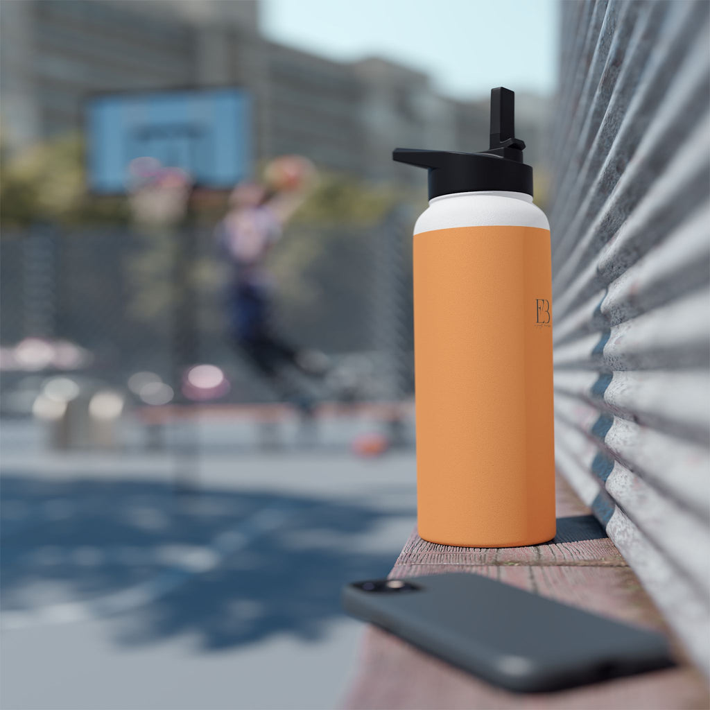 Matte orange-gold stainless water bottle with black sports lid, standing outdoors