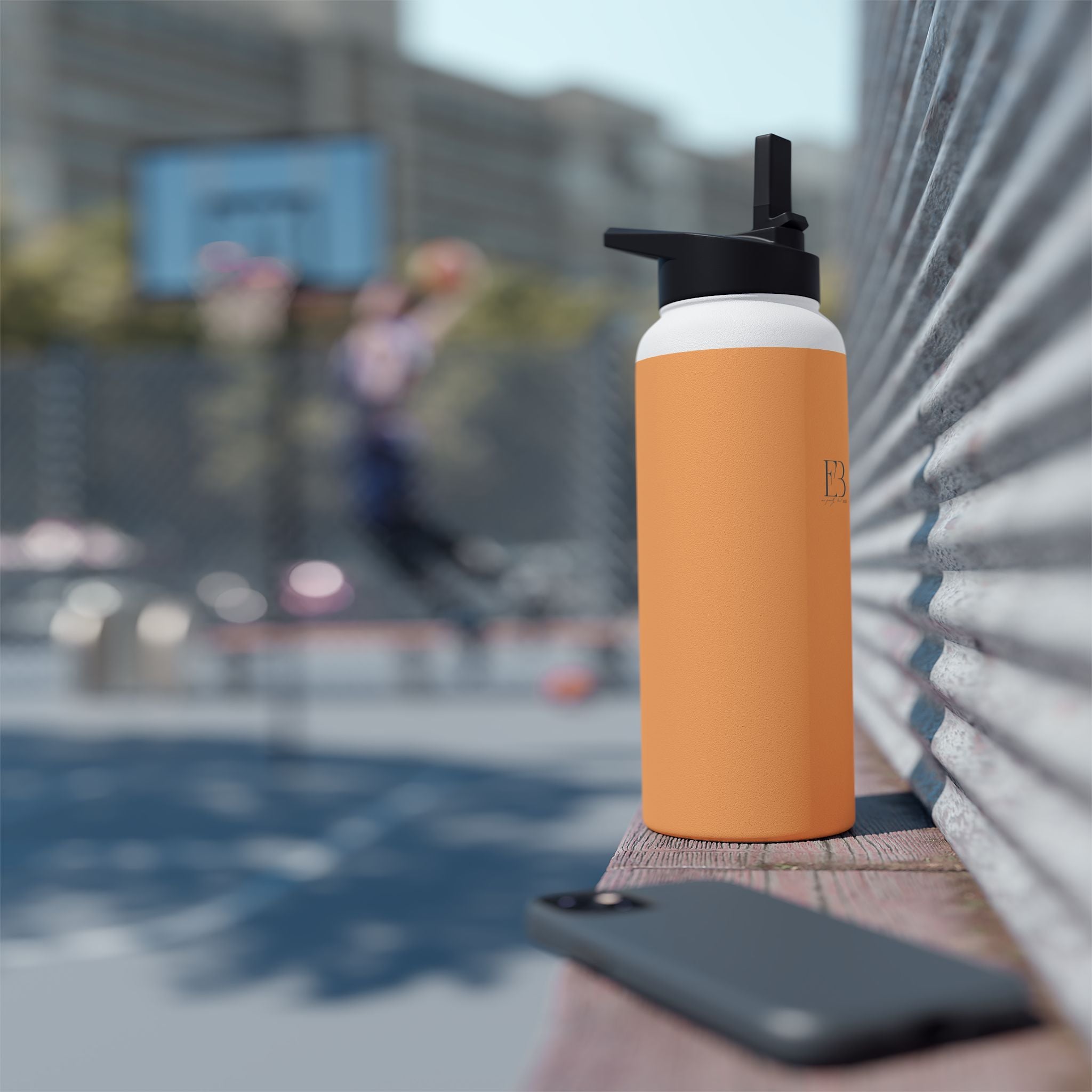 Matte orange-gold stainless water bottle with black sports lid, standing outdoors