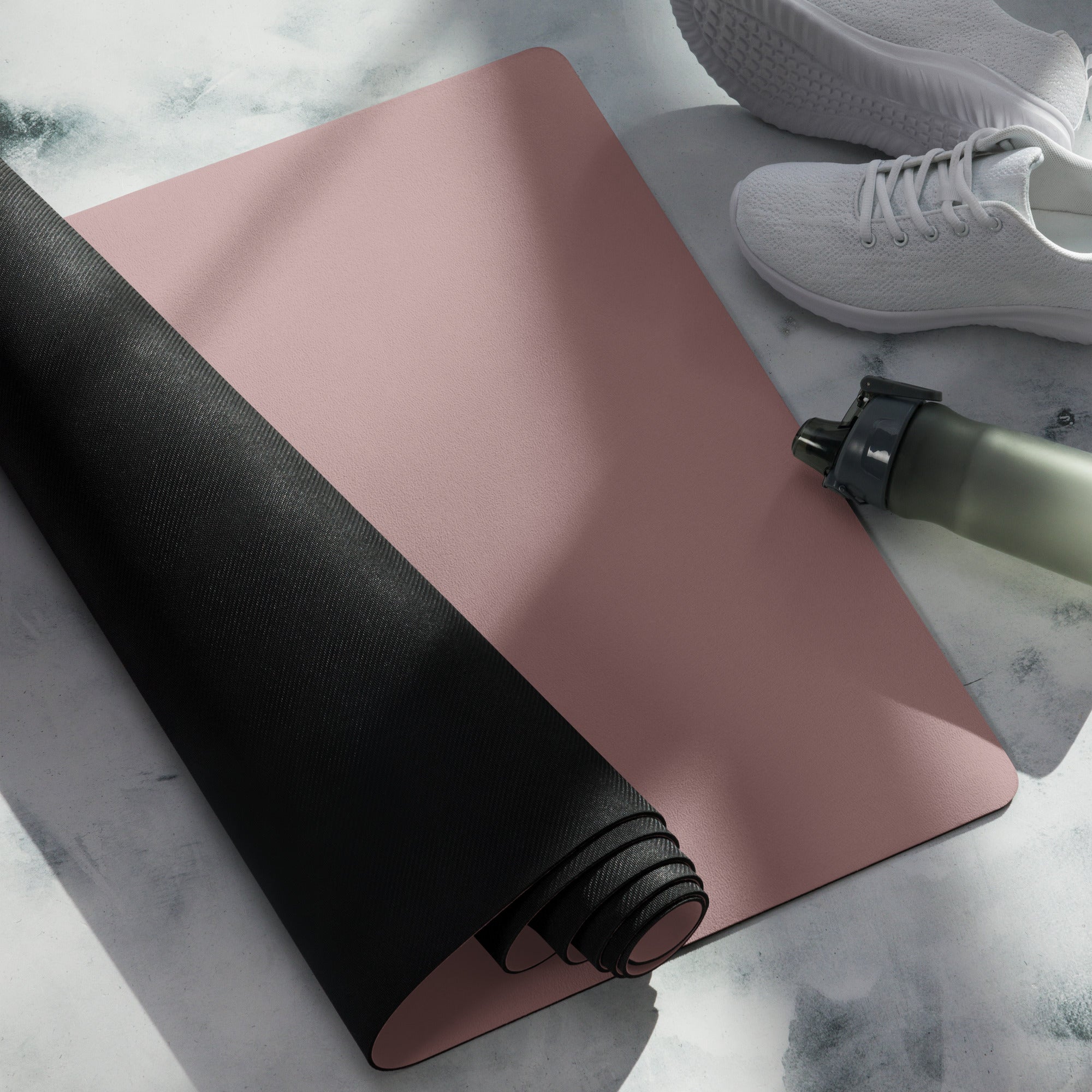 Mauve yoga mat with black rolled side and water bottle on top.
