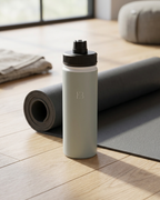 Sage insulated water bottle with black lid standing on yoga mat, embossed EB logo