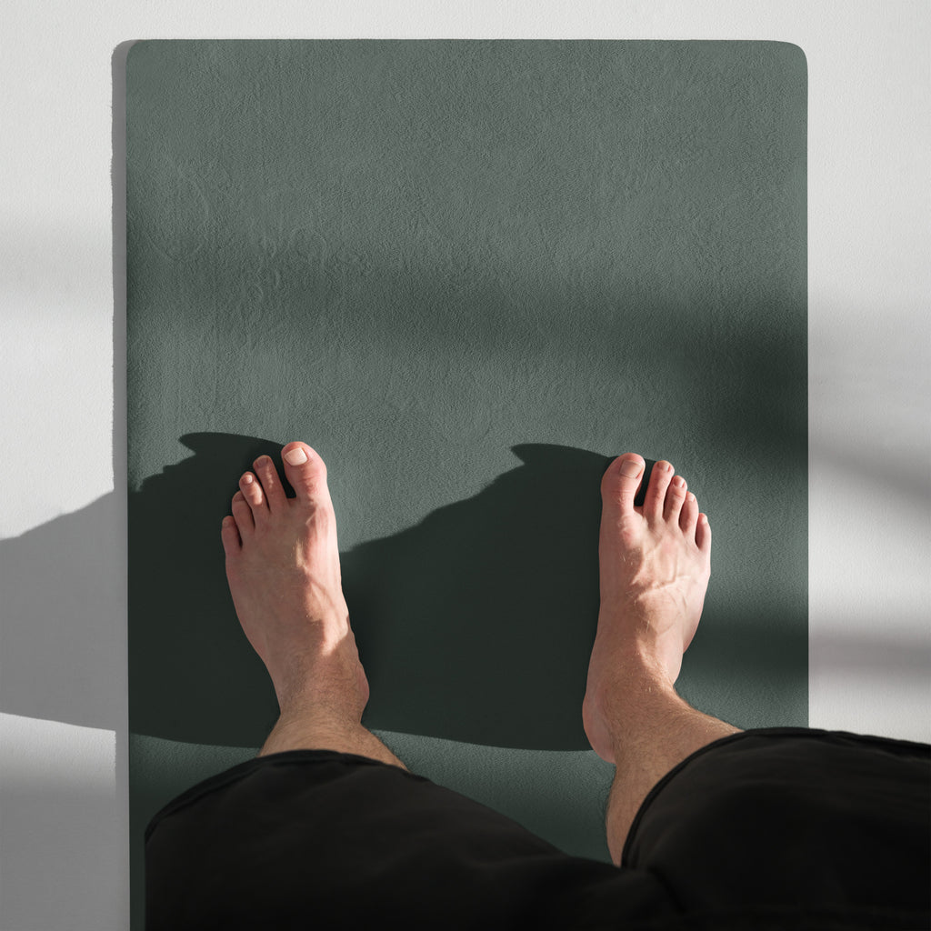 Cypress green yoga mat under bare feet, showing textured slip-resistant surface.
