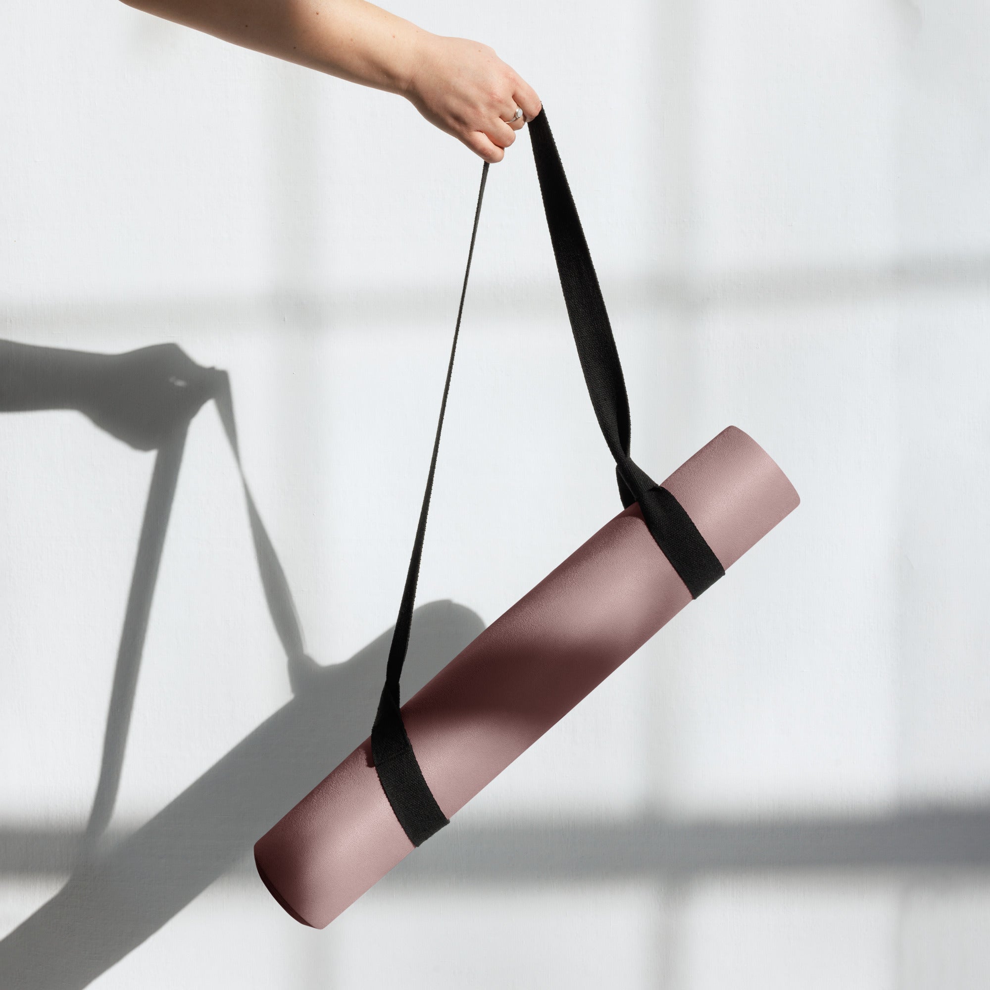 Rolled clay pink yoga mat lifted by a black carry strap