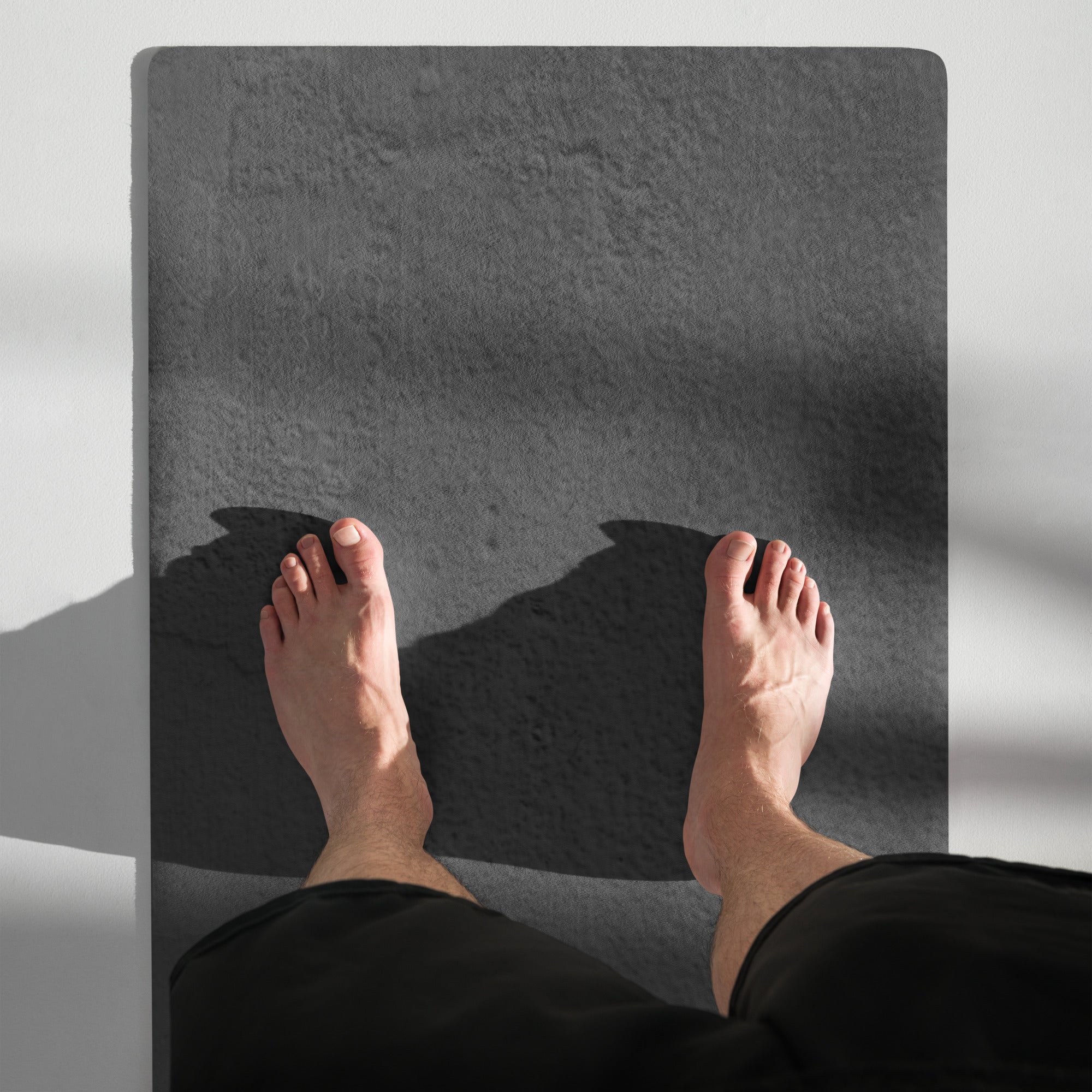Dark gray yoga mat with two bare feet and textured surface. Eco Black Dark gray natural rubber yoga mat with Suede top 