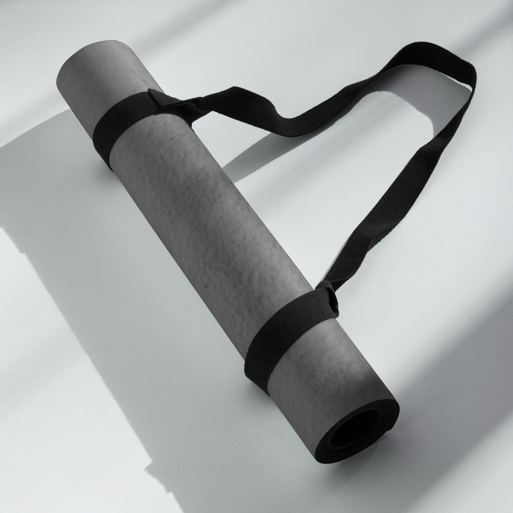 Rolled dark gray yoga mat secured with a black strap. Eco Black Dark gray natural rubber yoga mat with Suede top 