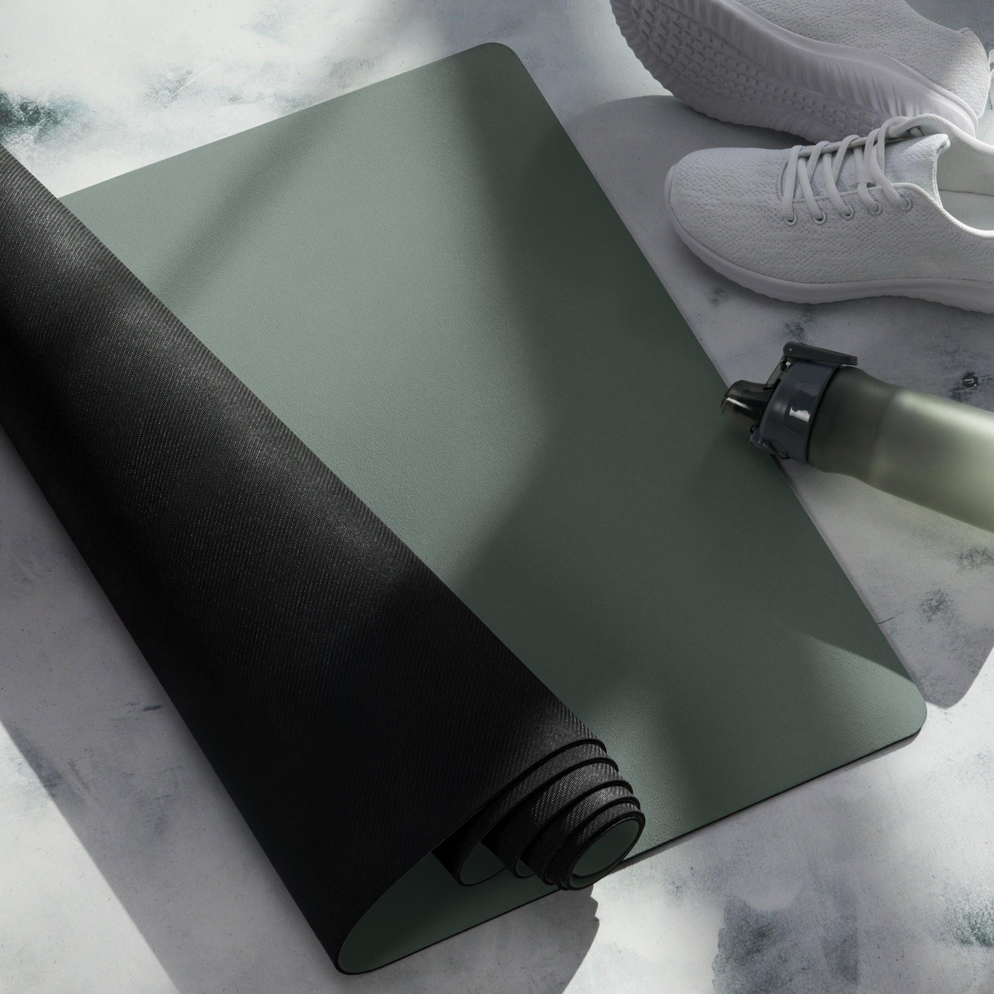 Rolled cypress green yoga mat with black edge banding and a bottle nearby.