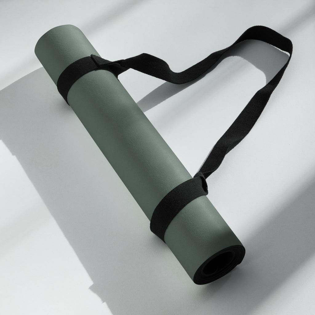 Rolled cypress green yoga mat secured with a black carrying strap.