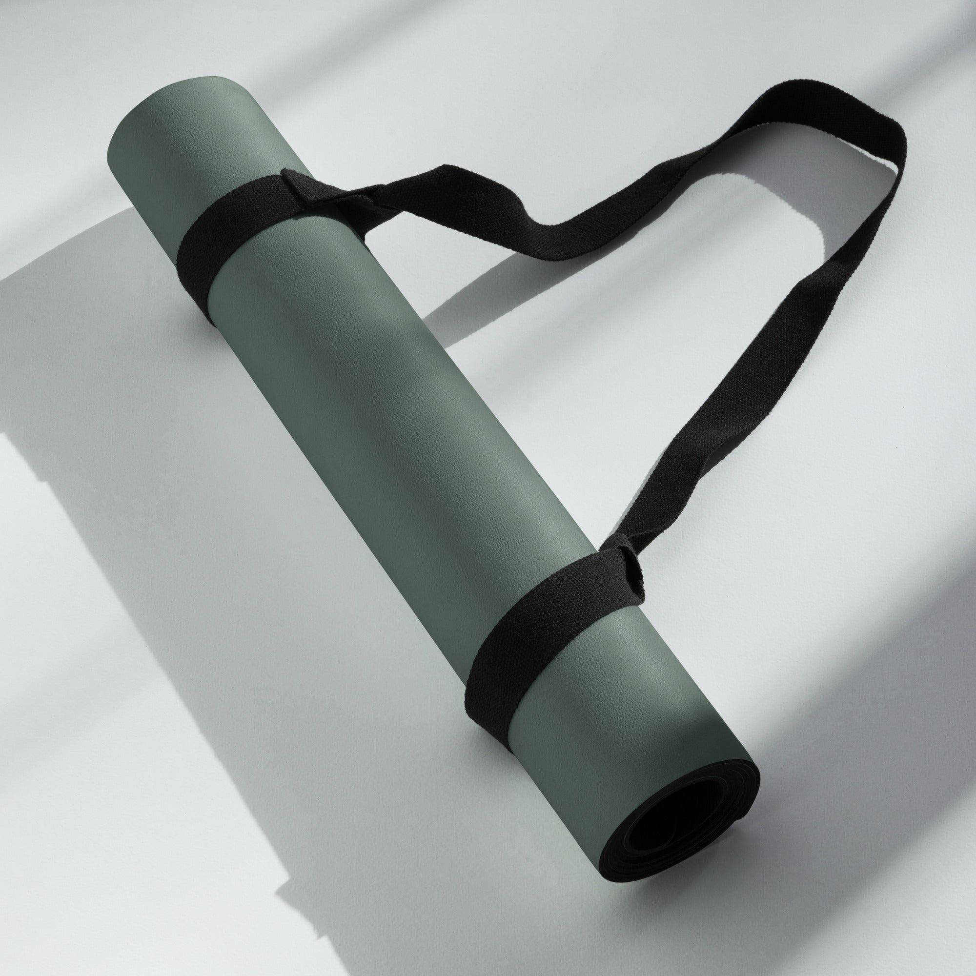 Rolled cypress green yoga mat secured with a black carrying strap.