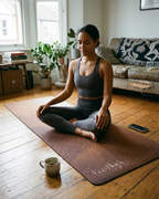 Brown natural rubber yoga mat laid flat with a seated yoga pose; logo visible near bottom.