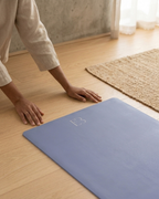 Pale iris yoga mat with embossed logo, pressed flat with hands to test grip.