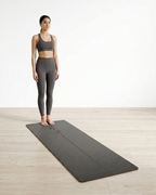 Dark gray yoga mat on wood floor with person standing pose