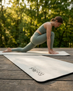 Light gray yoga mat on wooden deck, logo visible near the front edge.