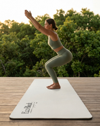 Light gray yoga mat on wooden deck, with printed logo at the corner.