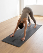 Dark gray yoga mat on floor with person in downward dog pose