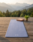 Pale iris yoga mat laid flat outdoors with embossed logo near center.