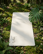 Light gray yoga mat lying on green moss, with printed logo near one corner.