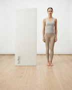 Light gray yoga mat standing upright on floor, with printed logo at the bottom.