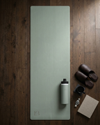 Sage green yoga mat with logo mark at bottom edge.