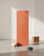 Orange yoga mat propped upright with embossed brand text.