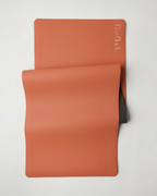 Orange yoga mat folded flat with a black backing layer behind it.