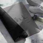 Black natural rubber yoga mat, rolled with textured grip and embossed logo on top.