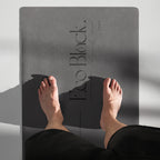 Black yoga mat with feet placed on it during a stretching pose.