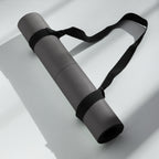 Rolled black yoga mat with a black carry strap looped around it.