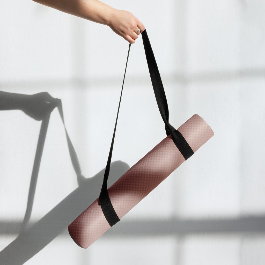 Yoga mat being lifted with black carry strap around the rolled mat