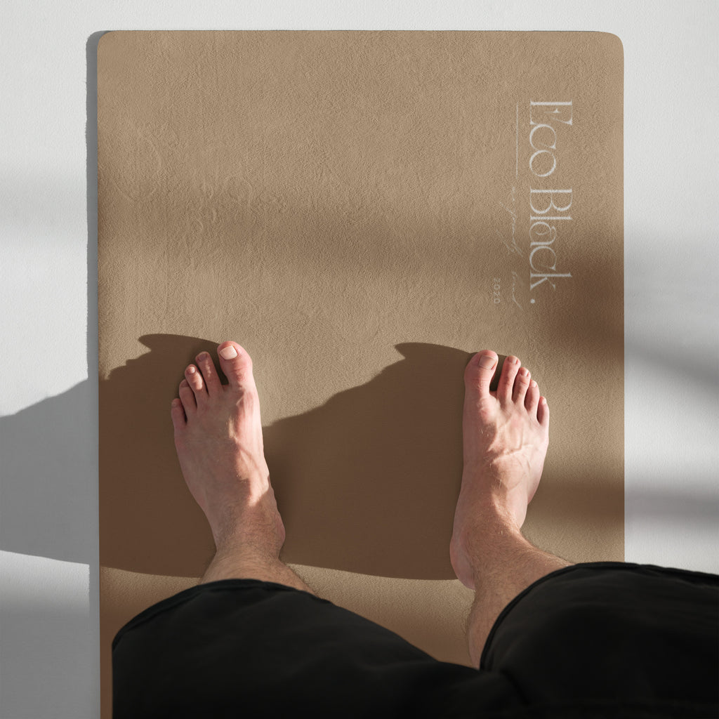 Natural rubber yoga mat under bare feet, tan surface with white logo.