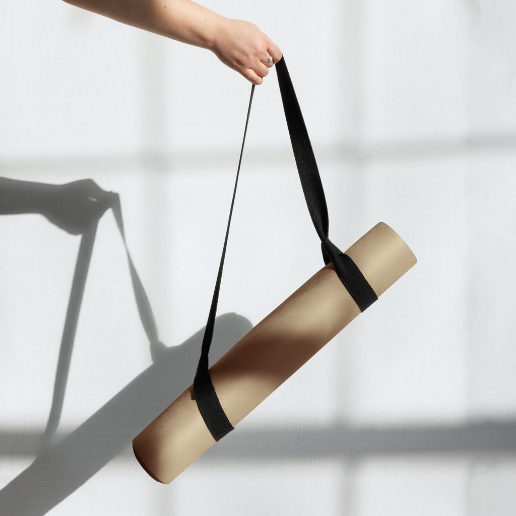 Tan yoga mat being carried with a black strap around the roll.