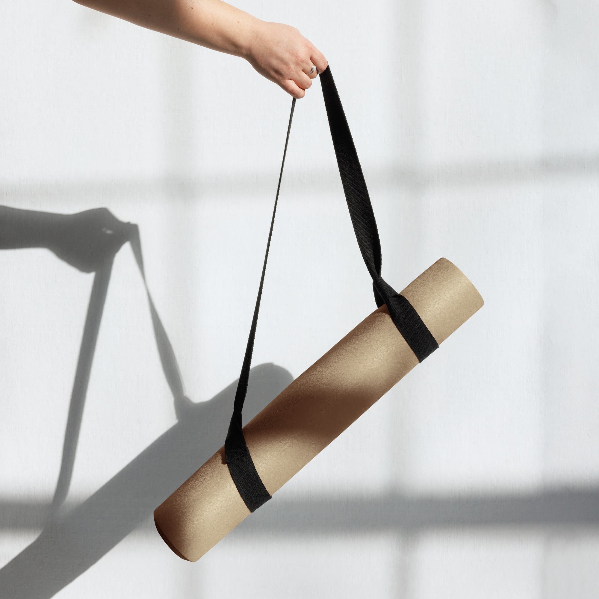 Tan yoga mat being carried with a black strap around the roll.