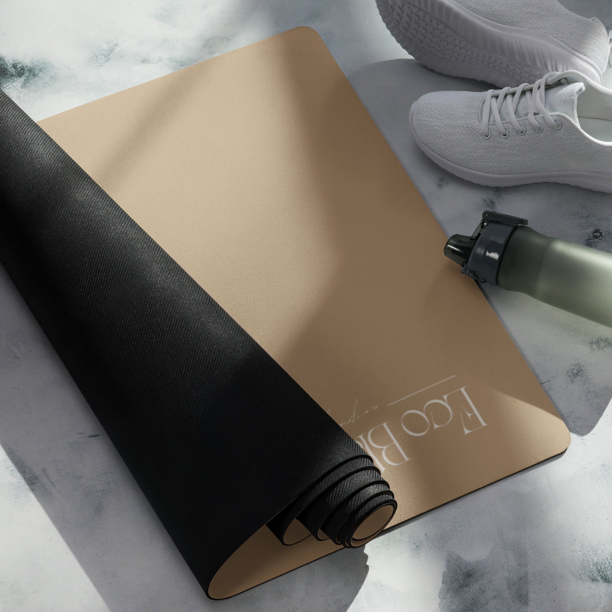 Tan yoga mat with white logo and a dark rolled section with elastic band.