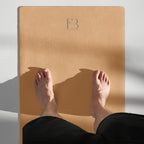Gold yoga mat with FB logo while seated with feet on the mat