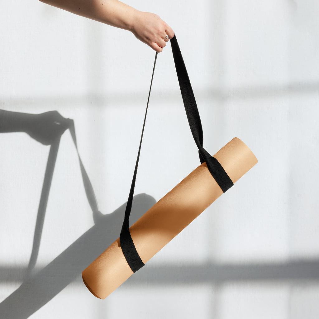 Gold natural rubber yoga mat with black carry strap, held rolled up