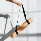 Gold natural rubber yoga mat with black carry strap, held rolled up
