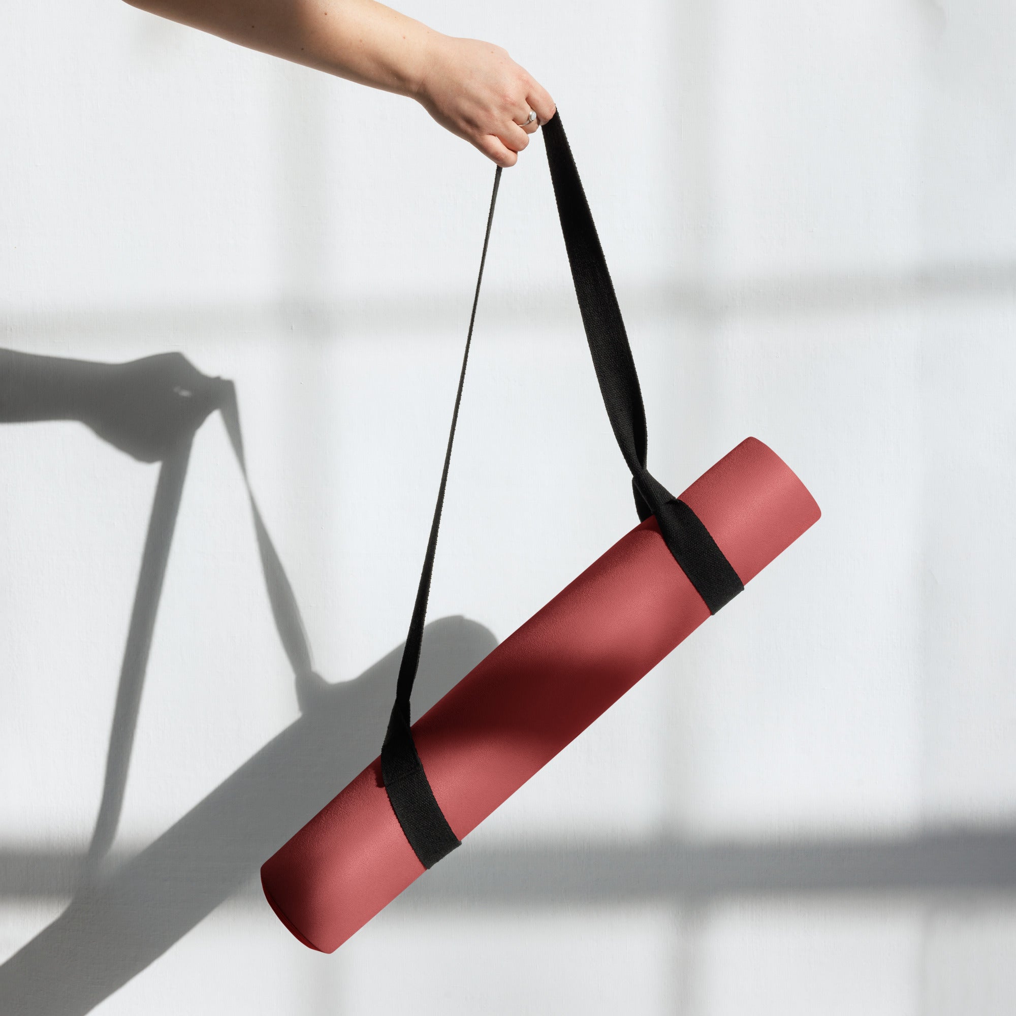 Crimson yoga mat with black carry strap held upright