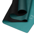 Deep teal yoga mat with black underside edge and rolled section detail.