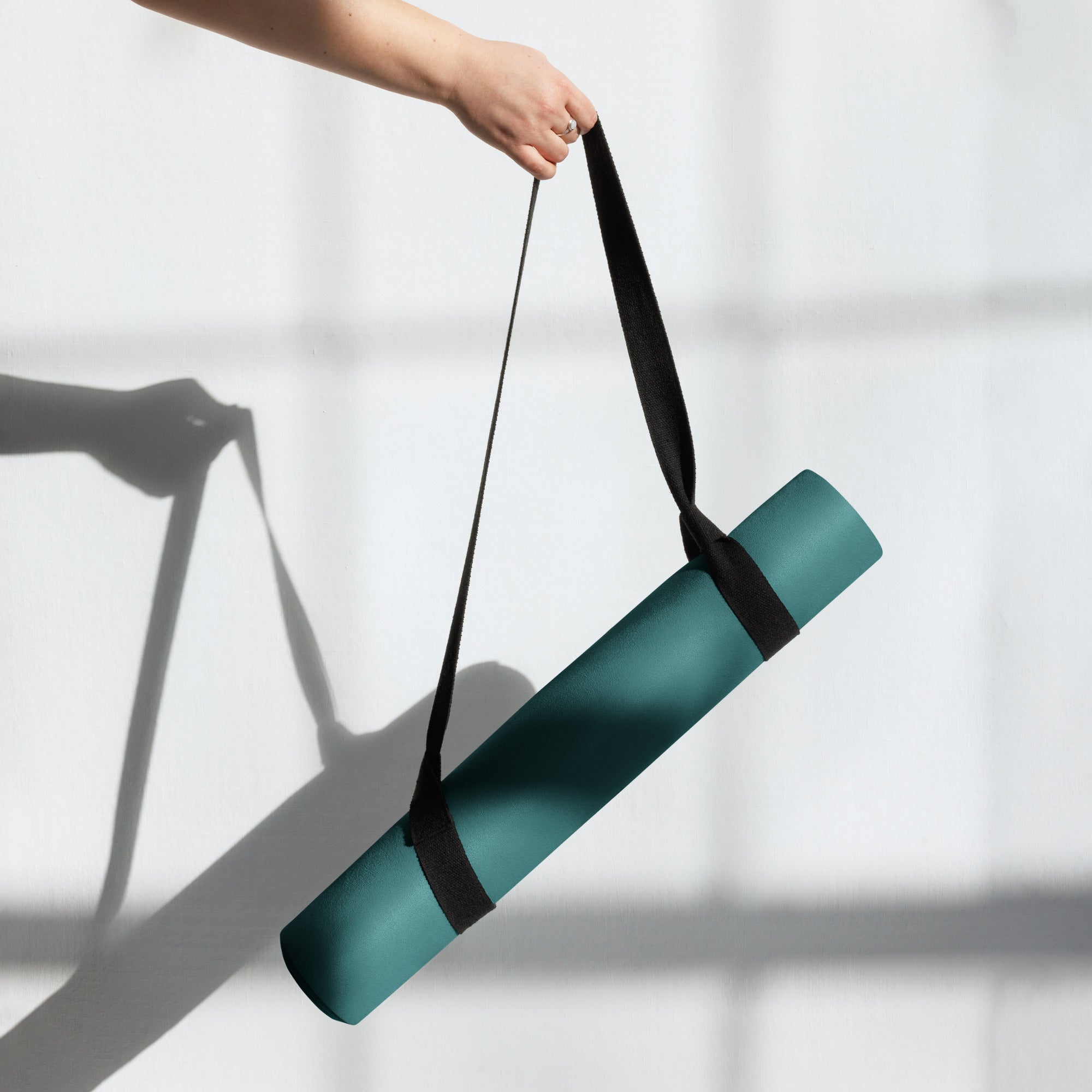 Deep teal natural rubber yoga mat being lifted using a black carrying strap.