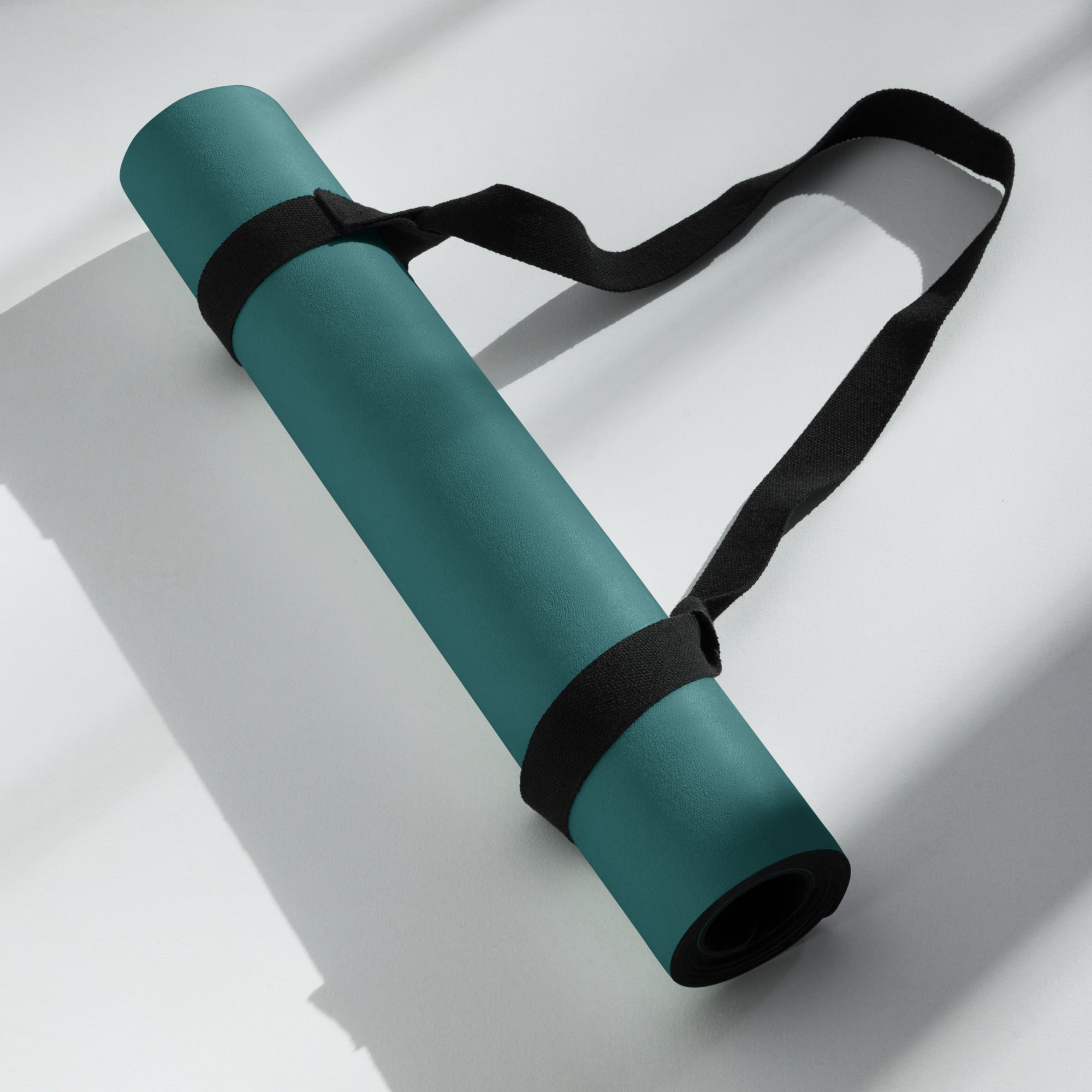 Deep teal natural rubber yoga mat with black straps, folded with rolled edge visible