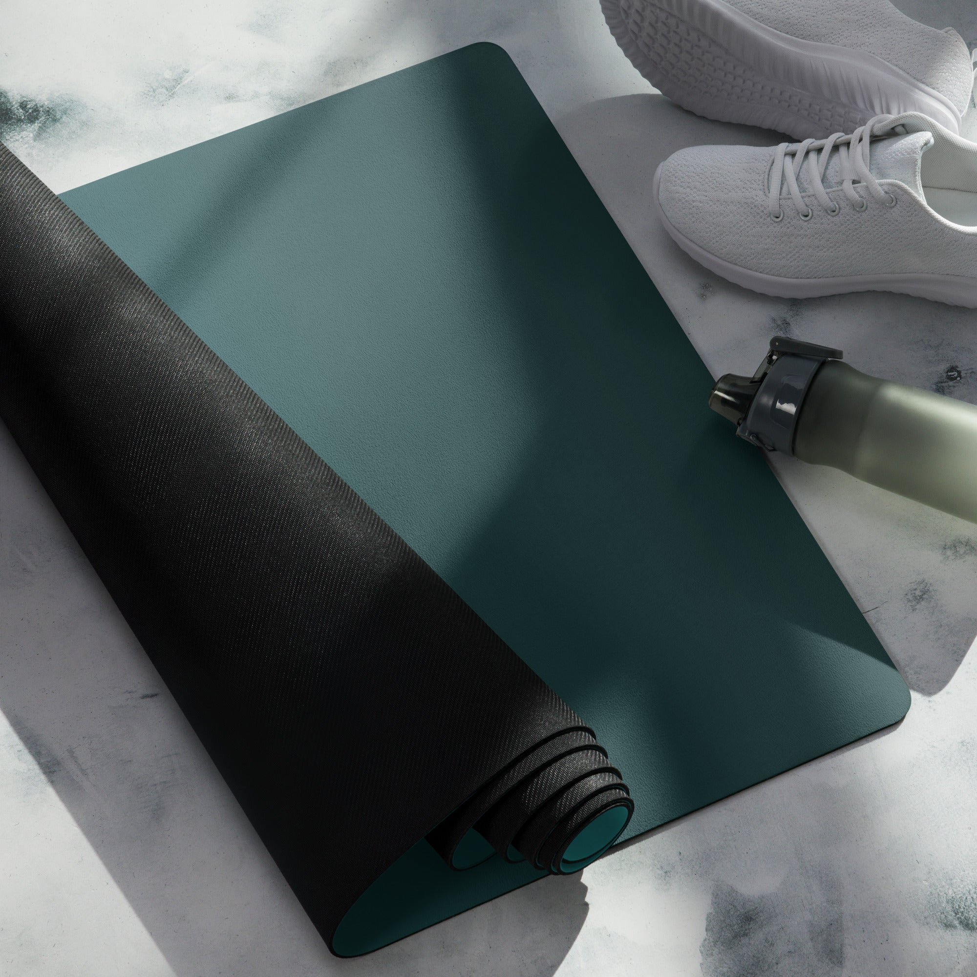 Teal natural rubber yoga mat rolled and folded with black grip strap detail
