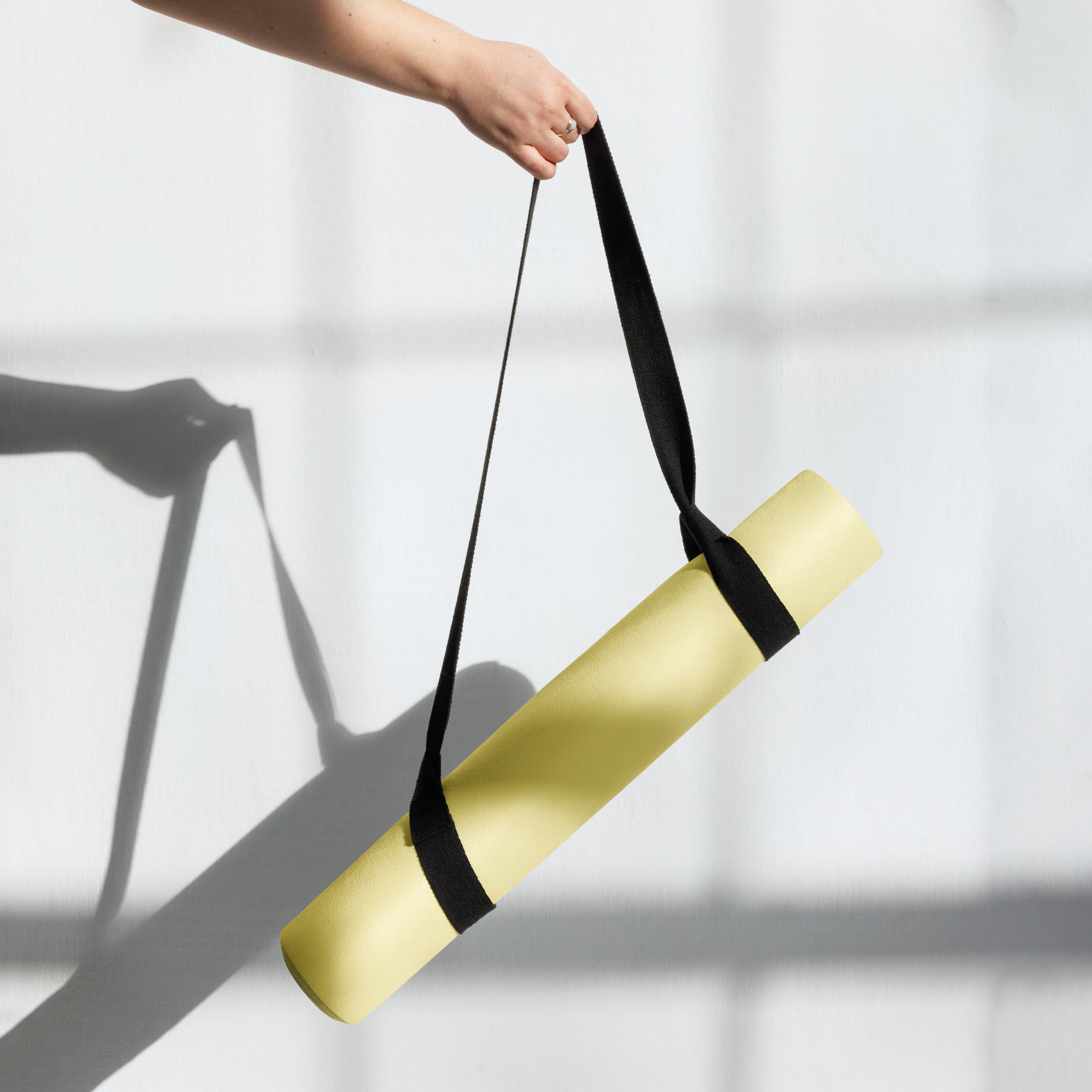 Yellow yoga mat being carried with a black strap held upward.