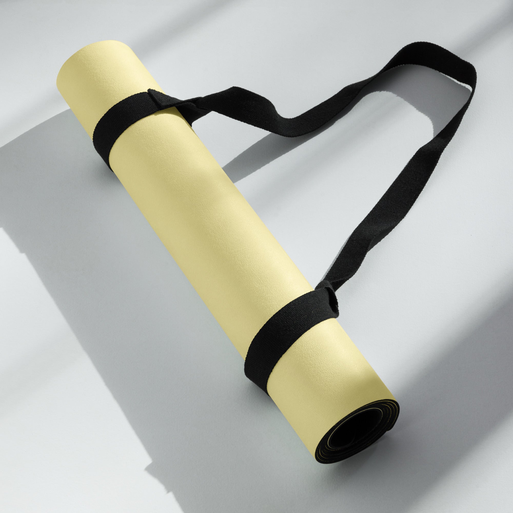 Yellow yoga mat with black carrying strap laid out flat.