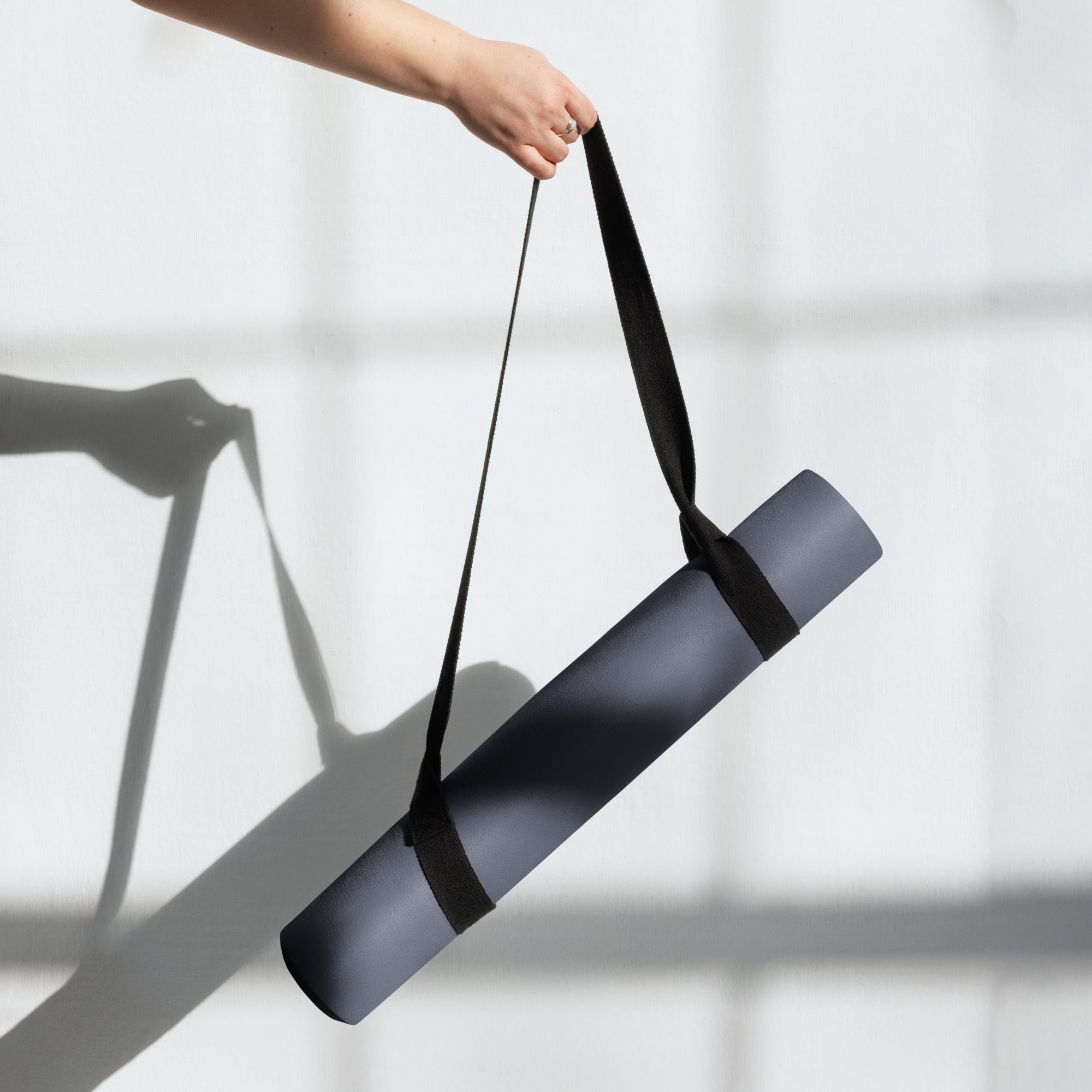 Slate blue yoga mat being held with a black carrying strap