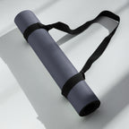 Rolled slate blue yoga mat with black strap, lying on a white surface
