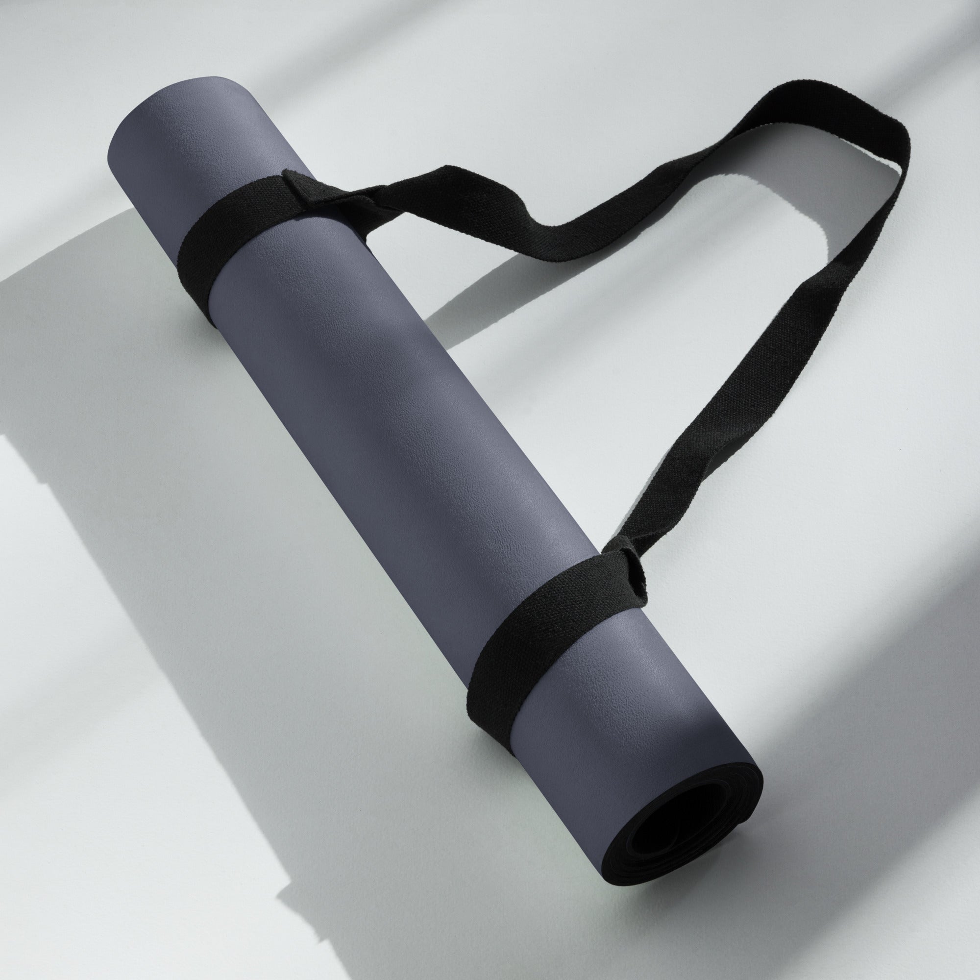 Rolled slate blue yoga mat with black strap, lying on a white surface