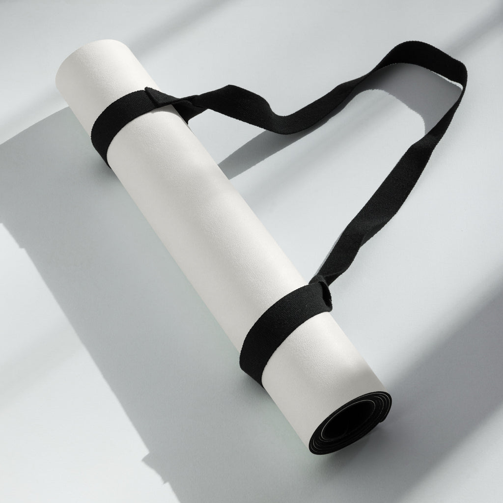Cream yoga mat rolled with black carry strap tied around the roll