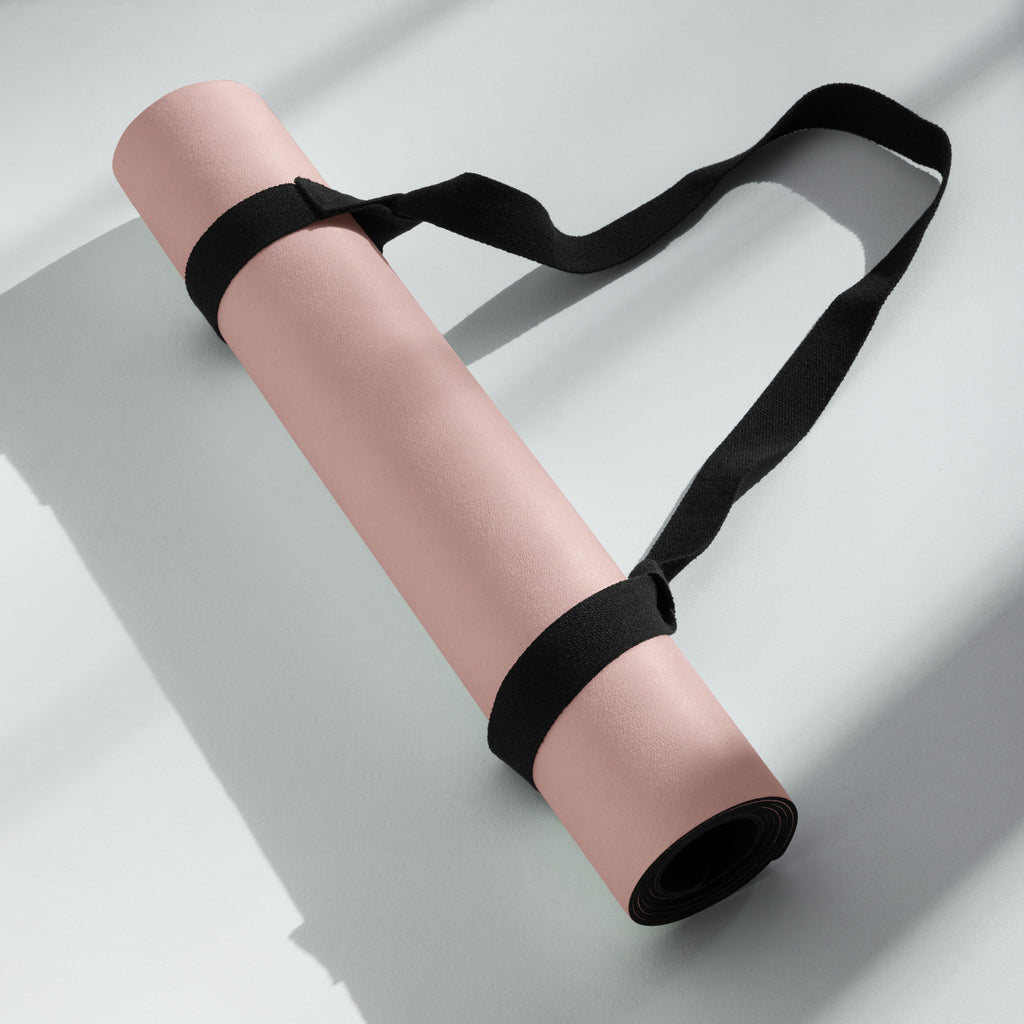 Rolled natural rubber yoga mat tied with black strap, violet-pink color