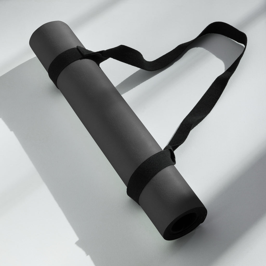 Black yoga mat rolled with black carry strap, folded for compact storage.