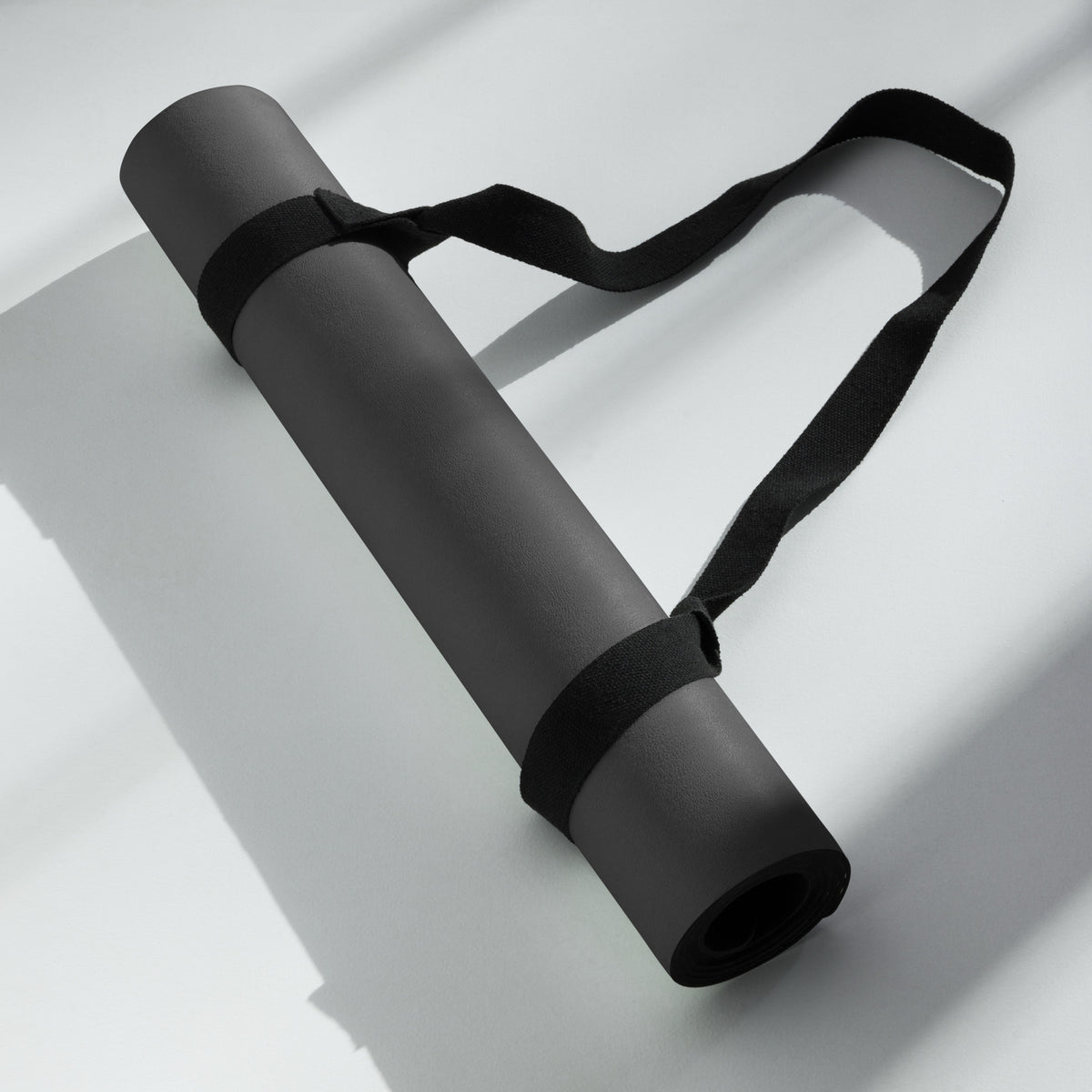 Black yoga mat rolled with black carry strap, folded for compact storage.