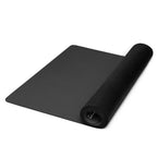 Black yoga mat unrolled with rolled end curling up, showing thickness and edge.