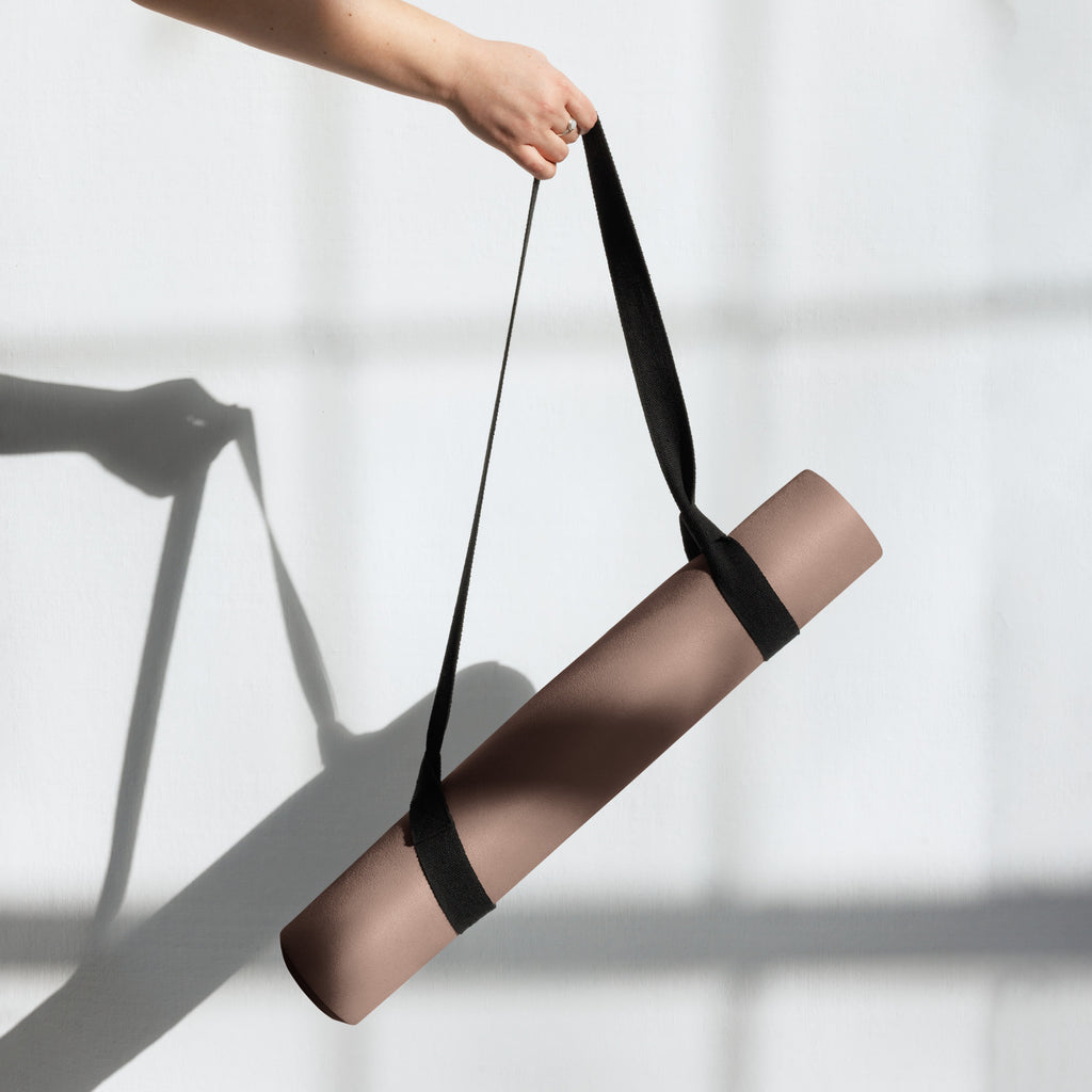 Chocolate yoga mat with black handle strap attached for carrying